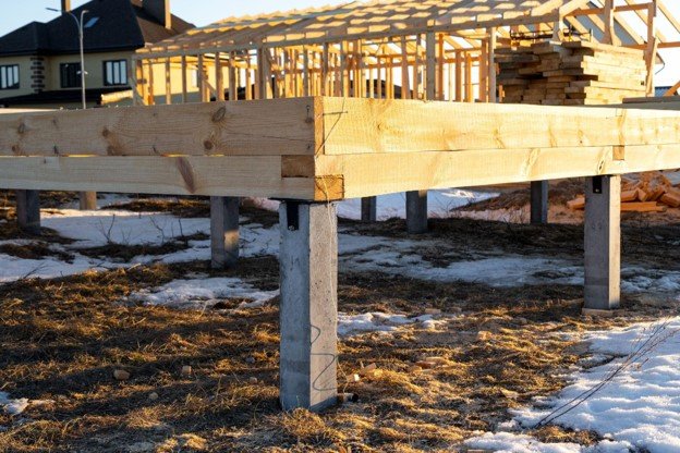 Custom wood deck framing supported by concrete posts during residential deck construction.