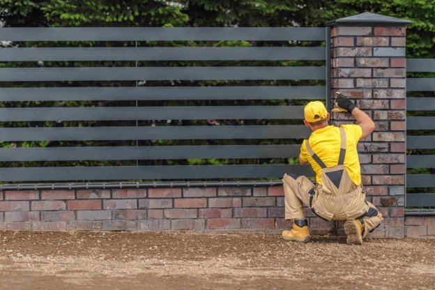 Professional contractor installing a modern horizontal fence with brick columns around a property