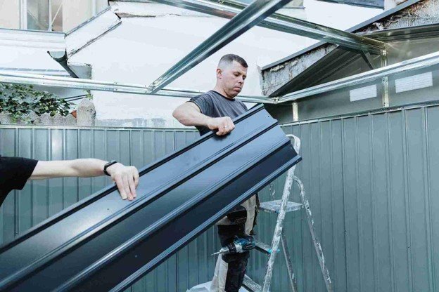Two professional workers doing patio enclosure construction while holding a metal.