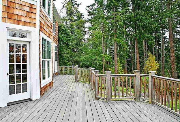 Professionally refinished residential wood deck with restored decking and railings overlooking a wooded backyard.