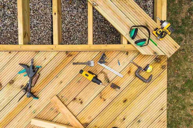 Deck repair tools and power drill arranged on wood decking during a residential repair project.