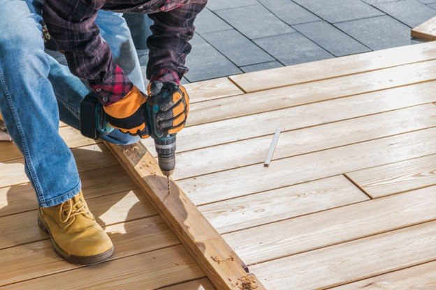 A professional man working on wood deck construction with a power tool on hand.