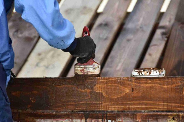 Contractor applying protective stain to wood boards during a residential deck replacement project.