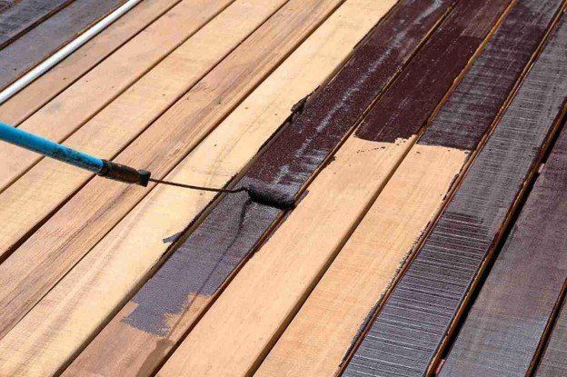 Roller applying dark wood stain to deck boards during a residential deck refinishing project.