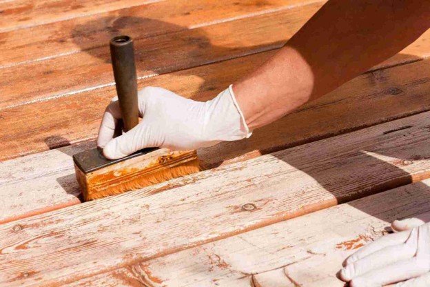 Contractor applying wood stain to worn deck boards as part of a professional deck refinishing project.