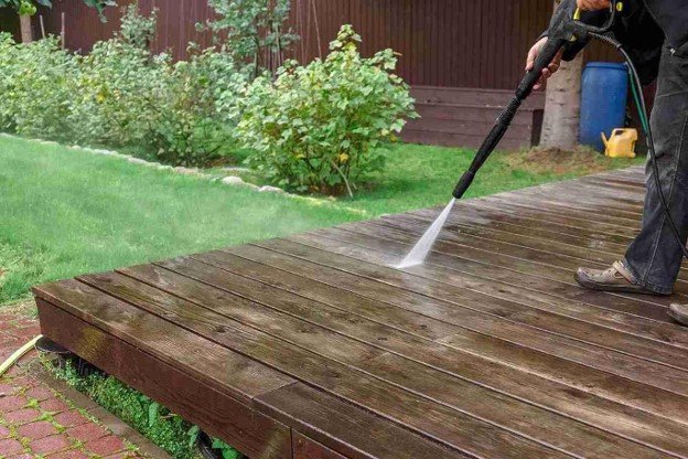Professional pressure washing a weathered wooden deck before refinishing