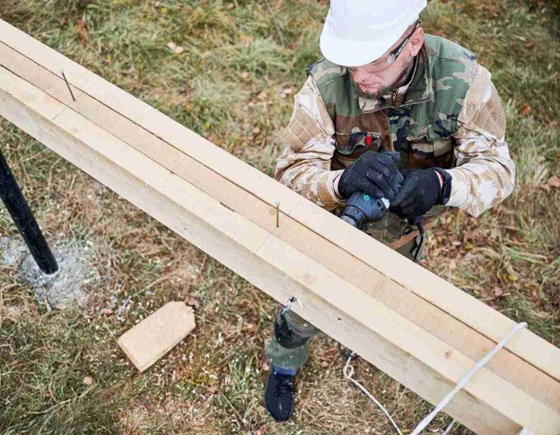 Contractor cutting lumber with a power tool during a residential wood fence building project.