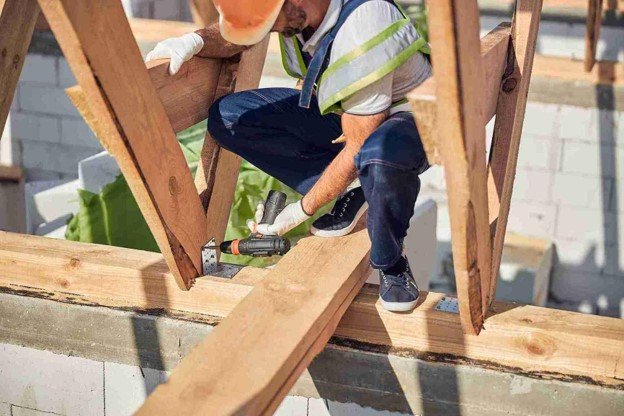 Contractor securing wood framing with a power drill during an outdoor pergola construction project.