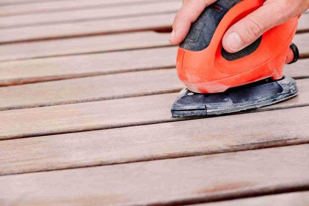 Worker sanding wooden deck boards to remove the old finish and prepare the surface