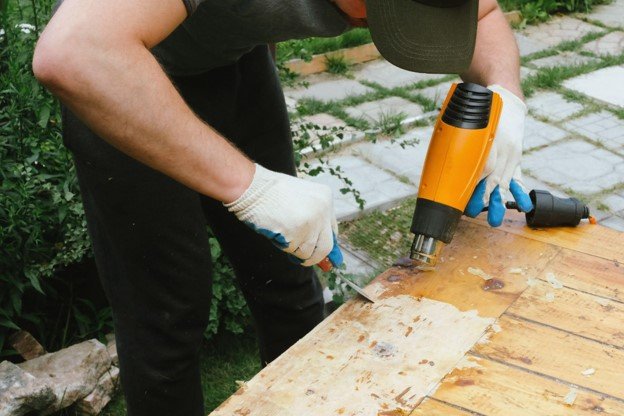 A professional repairing an old deck with blower and scratch tool.