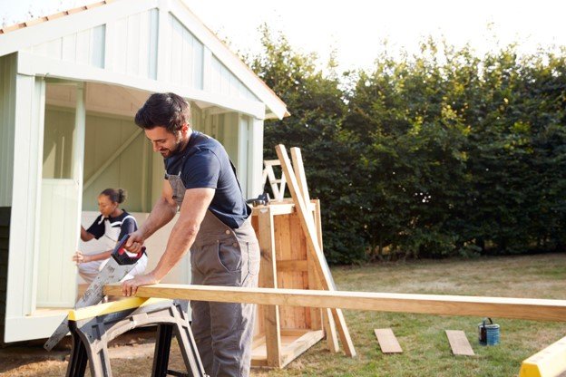 A professional working on outdoor kitchen construction sawing a wood.