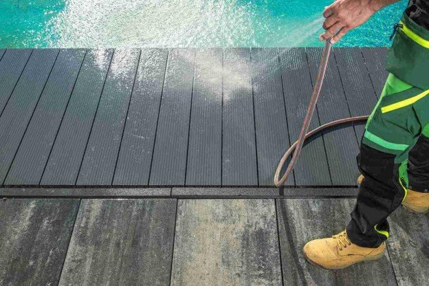 Deck cleaning professional washing a composite pool deck with a high-pressure water hose